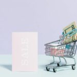 Savings Cart - Sale Sign Beside A Miniature Shopping Cart