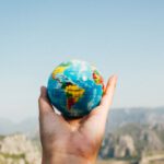 Travel Insurance - Person Holding World Globe Facing Mountain