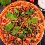 Spices And Herbs - A pizza with mushrooms, spinach and tomatoes on a black table