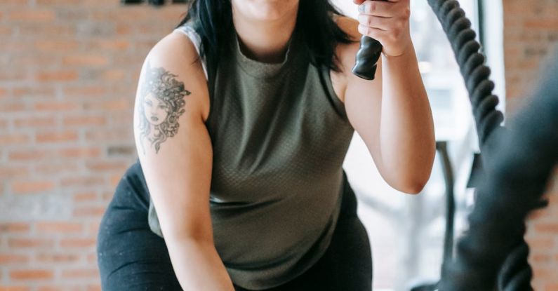 Activewear - Low angle of concentrated female in sportswear exercising with heavy battle ropes during intense functional training