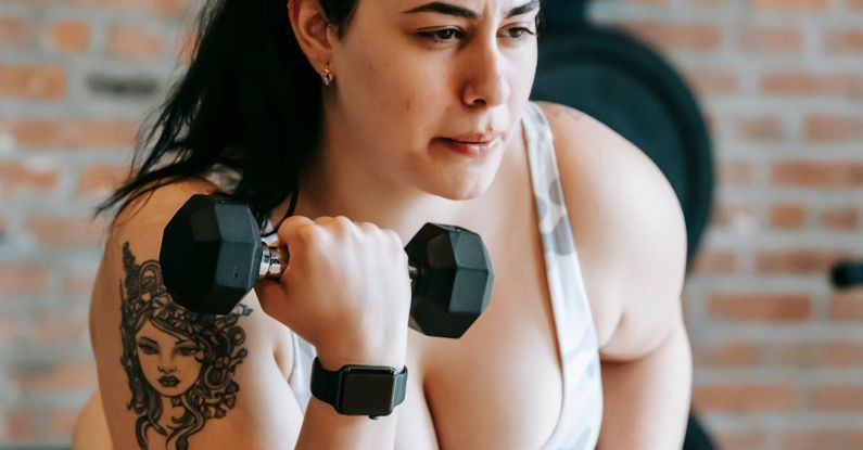 Strength Equipment - Concentrated woman in sportswear sitting on bench and lifting dumbbell during weight loss workout in gym with fitness equipment