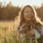 Pet Apparel - Woman in White Long Sleeve Shirt Sitting on Green Grass Field