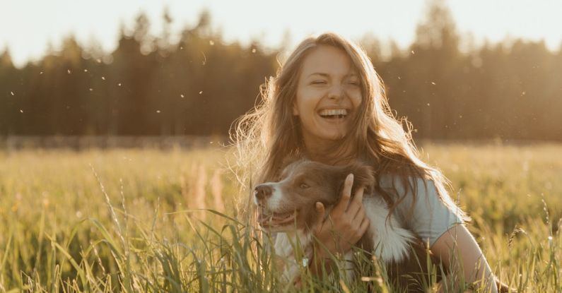 Pet Apparel - Woman in White Long Sleeve Shirt Sitting on Green Grass Field