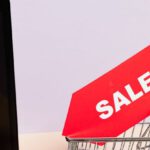 Electronics Sale - A Red Sale Tag on a Miniature Shopping Cart Placed on a Macbook Laptop