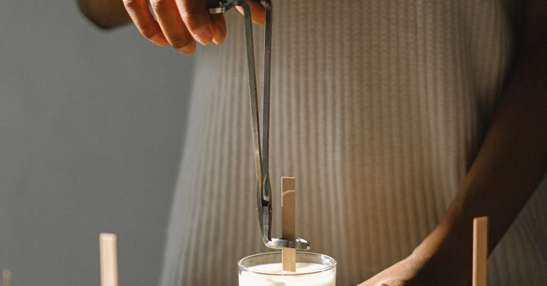 DIY Workspace - Unrecognizable African American female standing at wooden table with candle and steel wick dipper in light room with sunlight