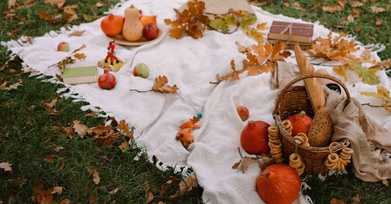 Top Products - From above of ripe exotic red kuri squashes with pumpkins and wicker basket with fresh bread arranged on blanket with books and scattered dry leaves in autumn park