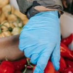 Viral Products - Crop anonymous customer in protective gloves picking red peppers from container while buying goods on farm market during coronavirus pandemic