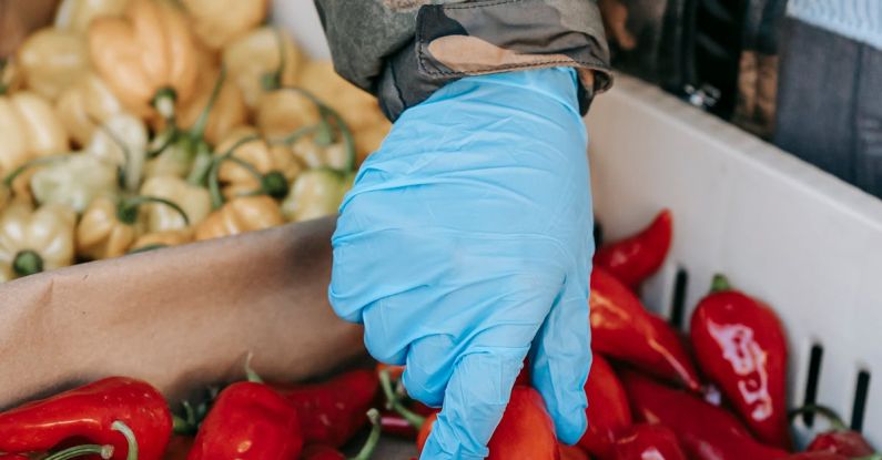 Viral Products - Crop anonymous customer in protective gloves picking red peppers from container while buying goods on farm market during coronavirus pandemic