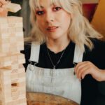 Game Changers - A woman sitting on a couch with a giant wooden tower