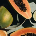 Vegan Trends - Top view of halves of ripe papaya together with oranges and limes placed on green round dishes and green fabric on white background