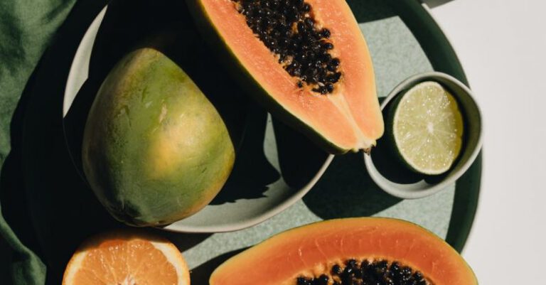 Vegan Trends - Top view of halves of ripe papaya together with oranges and limes placed on green round dishes and green fabric on white background