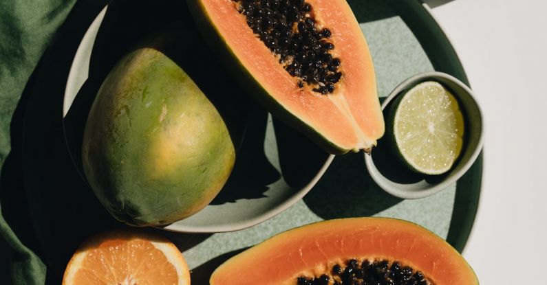 Vegan Trends - Top view of halves of ripe papaya together with oranges and limes placed on green round dishes and green fabric on white background