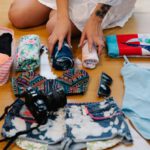 Travel Essentials - A Person Sitting on a Wooden Floor while Preparing Travel Essentials