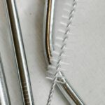 Eco Appliances - Top view composition of stainless steel straws and brush arranged on white bag on table