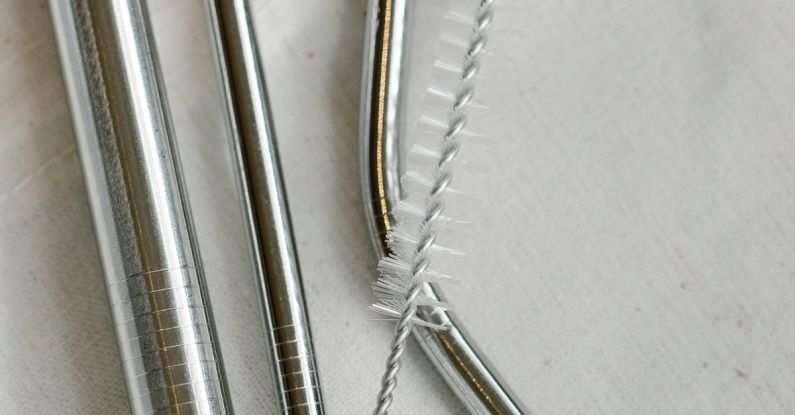 Eco Appliances - Top view composition of stainless steel straws and brush arranged on white bag on table