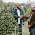 Holiday Deals - Cheerful African American dad clapping had of teenage son while standing in farm with Christmas trees