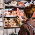 Beauty Boxes - Woman in Gray Jacket Standing in Front of White Wooden Shelf