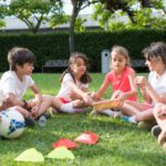 Outdoor Play - Kids Playing while Sitting on the Green Grass