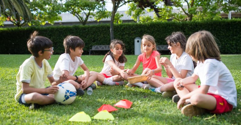 Outdoor Play - Kids Playing while Sitting on the Green Grass