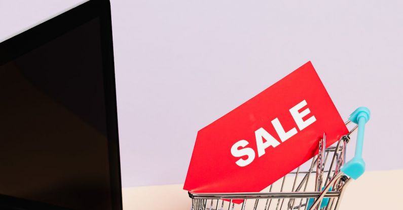 Electronics Sale - A Red Sale Tag on a Miniature Shopping Cart Placed on a Macbook Laptop